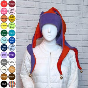 Peut inclure: Un chapeau de bouffon à plusieurs pointes en tissu polaire violet et orange. Le chapeau présente trois longues pointes pendantes, chacune terminée par une petite clochette métallique. Il inclut une large bande violette ajustée sur le front.