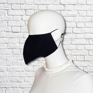 Pode incluir: Uma máscara facial preta sólida com uma projeção pontiaguda em forma de bico que se estende a partir do centro. A máscara apresenta alças elásticas pretas finas para as orelhas, presas com pequenos botões de ajuste circulares claros.