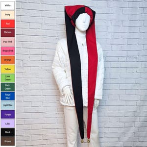 May include: A jester hat featuring a split design with one long black panel and one long red panel, each ending in a small gold bell. The hat is displayed on a white mannequin wearing a white quilted jacket and white pants, with a color chart.