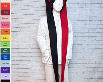 Puede incluir: Un gorro de bufón con un diseño dividido con un panel largo negro y un panel largo rojo, cada uno terminado en un pequeño cascabel dorado. El gorro se muestra en un maniquí blanco que viste una chaqueta acolchada blanca y pantalones blancos.