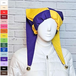 Puede incluir: Un gorro de bufón con un patrón de bloques de color vibrante que alterna paneles de tela amarilla y morada. El gorro tiene dos colas largas y puntiagudas que cuelgan a ambos lados, cada una terminada con un pequeño cascabel metálico dorado.