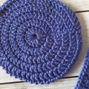 May include: A close-up of a crocheted circle in a deep blue color. The circle is made with a textured stitch pattern.