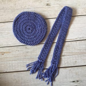 May include: A purple crocheted headband with a matching circle. The headband has a fringe on each end.