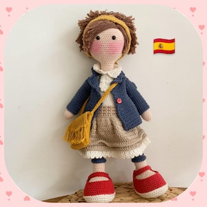 Puede incluir: Una muñeca de crochet que lleva una chaqueta azul, una falda marrón, un bolso amarillo y zapatos rojos. La muñeca tiene el pelo marrón y una diadema. Una pequeña bandera española está en el fondo.