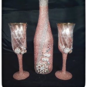May include: A set of two champagne flutes and a champagne bottle, all decorated with pink glitter and rhinestones. The flutes are engraved with the words "Mrs. & Mr. Doralynn".
