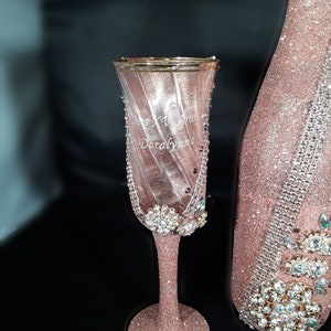 May include: A pink champagne flute with a gold rim and a personalised inscription that reads "Miss XV anos Doralynne". The flute is decorated with glitter and rhinestones.