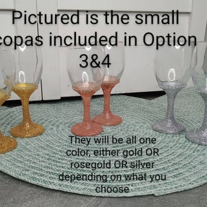 Puede incluir: Cuatro copas de vino peque&ntilde;as con purpurina dorada, oro rosa y plata. El texto "Pictured is the small copas included in Option 3&4" es visible en la imagen.