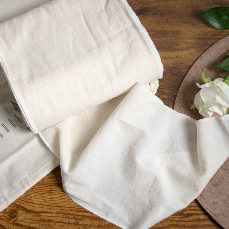 May include: A white cotton fabric runner with a slightly textured surface. The runner is folded in half and laid out on a wooden surface.