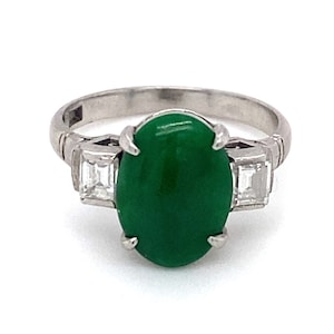 May include: A platinum ring with a green oval cabochon gemstone and two smaller square-shaped diamonds on either side.