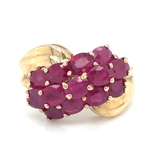 Pode incluir: Um anel de ouro com um aglomerado de pedras preciosas vermelhas rubi engastadas em uma banda torcida.
