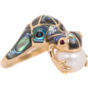 May include: A gold ring featuring a frog made of abalone shell holding a pearl. The frog has a red ruby eye.