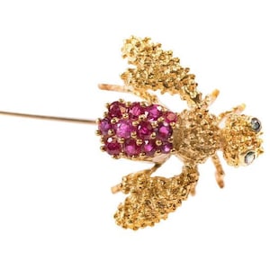 Op de afbeelding: Een gouden bij broche met robijn en diamant accenten. De bij is bevestigd op een gouden pin.