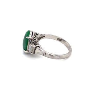 May include: A silver ring with a green oval gemstone and two smaller diamond-shaped gemstones. The ring is set in a delicate, intricate design.