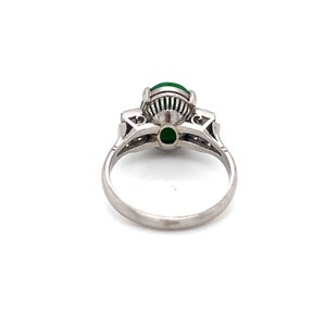May include: A platinum ring with a green gemstone surrounded by smaller diamonds. The ring is set with a delicate, intricate design.