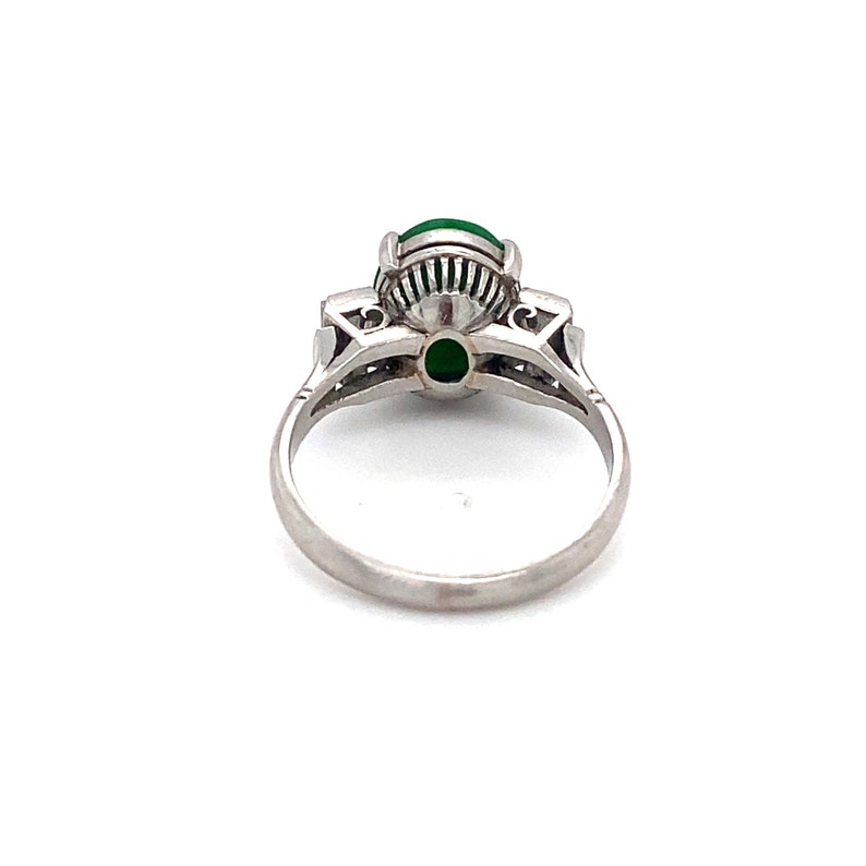 May include: A platinum ring with a green gemstone surrounded by smaller diamonds. The ring is set with a delicate, intricate design.