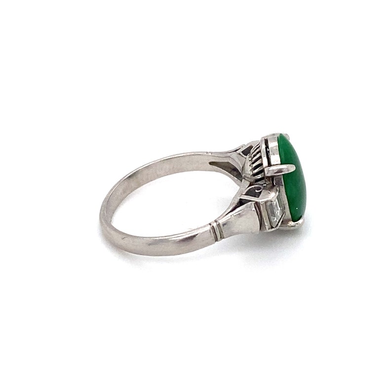 May include: A silver ring with a large green oval gemstone and smaller clear gemstones on the side.