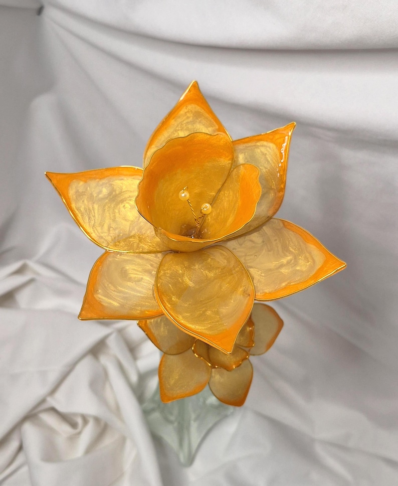 May include: A handcrafted decorative flower sculpture featuring translucent, swirling golden-yellow petals with vibrant orange edges. The center of the bloom displays two small, pale yellow stamens, creating a layered, multi-dimensional floral appearance.