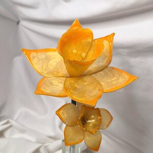 May include: A decorative flower sculpture featuring two blossoms with translucent, pearlescent cream-colored petals and vibrant orange edges. The larger top flower and smaller bottom flower both have delicate stamens in the center of their cups.