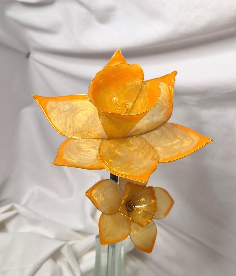 May include: A decorative flower sculpture featuring two blossoms with translucent, pearlescent cream-colored petals and vibrant orange edges. The larger top flower and smaller bottom flower both have delicate stamens in the center of their cups.