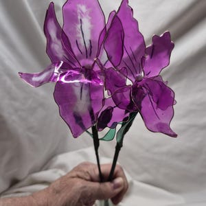 May include: Two artificial flowers with translucent, deep purple petals crafted from a thin, flexible material. Each flower features dark, wire-like stems and delicate, vein-like markings on the petals, creating a realistic, layered floral appearance.