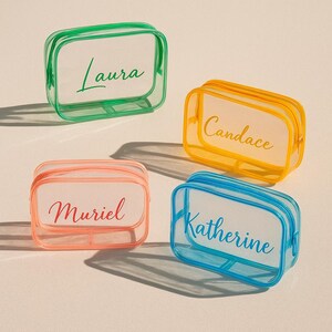 May include: Four clear, rectangular cosmetic bags with colored trim and zippers. Each bag has a different name printed on it: Laura, Candace, Muriel, and Katherine. The bags are in green, yellow, coral, and blue.