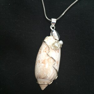 May include: A silver chain necklace with a white seashell pendant wrapped in silver wire. The pendant is accented with small white pearls and a silver charm.