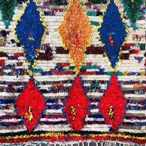May include: A colorful Moroccan rug with a white background and a pattern of red, blue, orange, and yellow diamonds. The rug has a fringe border.