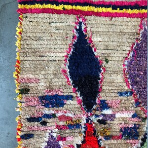 May include: A colorful Moroccan rug with a geometric pattern in shades of pink, blue, yellow, and red. The rug is made of wool and has a hand-woven texture.