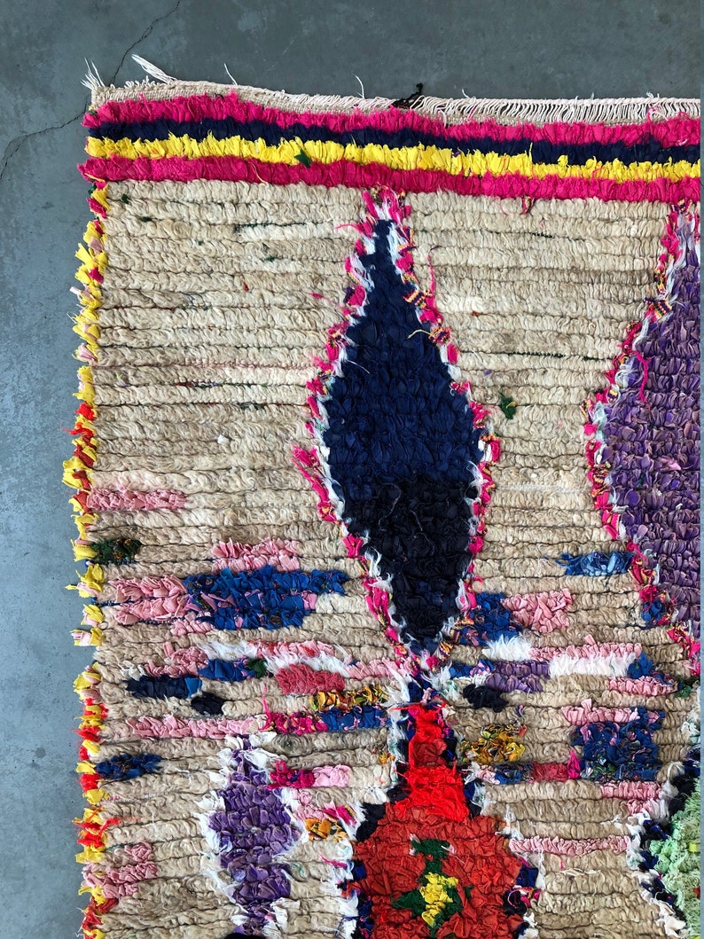May include: A colorful Moroccan rug with a geometric pattern in shades of pink, blue, yellow, and red. The rug is made of wool and has a hand-woven texture.