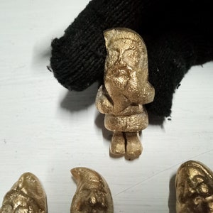 Puede incluir: Una colección de figuritas doradas, incluyendo una figura de Papá Noel, sobre una superficie blanca.
