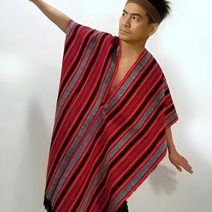 May include: A red, black, and grey striped poncho with a fringed hem. The poncho has a V-neck design. A brown headband is worn on the head.