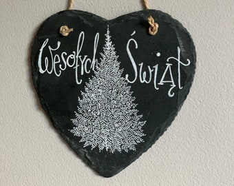 May include: A heart-shaped black slate sign with the words "Wesołych Świąt" in white script, and a white Christmas tree design. The sign is suspended by a natural rope.
