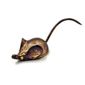 May include: A bronze mouse figurine with a long, curved tail. The mouse is lying on its side with its head turned to the side. The figurine has a distressed finish, giving it a vintage look.
