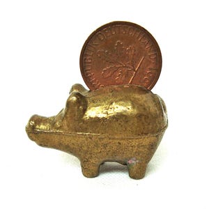 May include: A gold piggy bank with a coin slot on the back. A copper German coin is inserted into the slot.