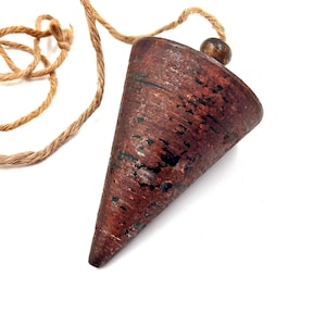 May include: A vintage plumb bob with a conical, reddish-brown body and a natural rope. The plumb bob has a wooden bead at the top where the rope is attached. The tool is used for establishing a true vertical.