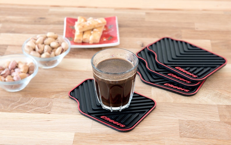 May include: Four black and red square coasters with the word "Cheers" printed on each. A glass of dark coffee sits on one of the coasters.