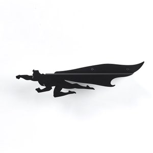 Op de afbeelding: Zwart metalen wandkunst die een superheld in vlucht afbeeldt, met een lange cape. Het silhouet is op een witte muur gemonteerd. Het kunstwerk is een gestileerde weergave van een vliegende figuur, perfect voor een kinderkamer.