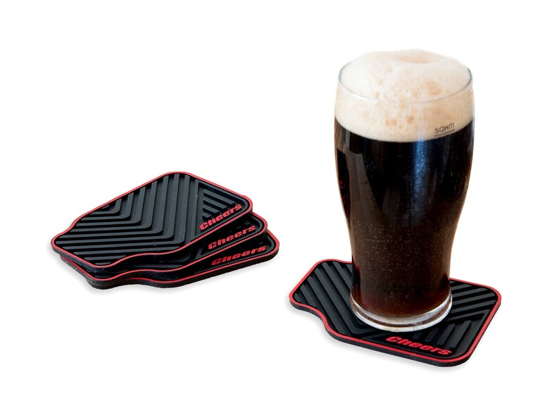 May include: Three black and red silicone coasters with the word "Cheers" printed on each. A glass of dark beer is sitting on one of the coasters.