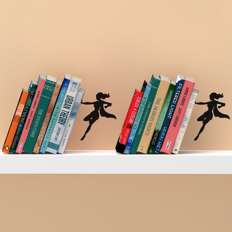 May include: A set of two black silhouette bookends shaped like a superhero with a cape. The bookends are holding up a stack of books on a white shelf.