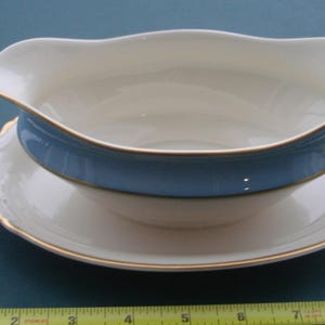 May include: A white porcelain gravy boat with a blue band and gold trim. The boat is sitting on a matching saucer.