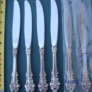 May include: Five silver dinner knives with ornate handles in a clear plastic package. The knives are in new condition and have a polished finish.