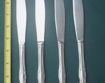 May include: Four silver dinner knives with ornate handles. The knives have a polished finish and are arranged in a row.
