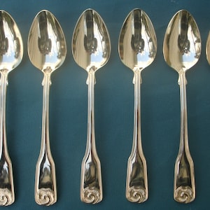 May include: Six gold-plated teaspoons with ornate handles. The spoons have a polished finish and are arranged in a row.