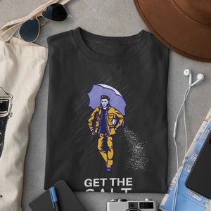 May include: Black t-shirt with a graphic of a person walking in the rain with an umbrella and holding a bag of salt. The text "GET THE SALT" is printed below the graphic.