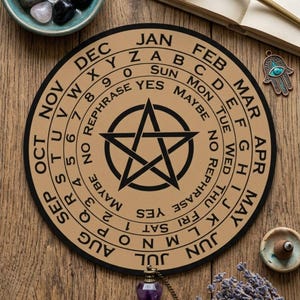 May include: A circular tan dowsing board featuring a black pentagram at the center, surrounded by concentric rings containing the alphabet, numbers 0-9, months of the year, and the words YES, NO, MAYBE, and REPHRASE, paired with a purple crystal pendulum.