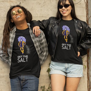 May include: Two people wearing black t-shirts with a graphic of a person holding an umbrella and the text "Get the Salt". The person on the left is wearing a plaid shirt and jeans. The person on the right is wearing a black leather jacket and denim shorts.