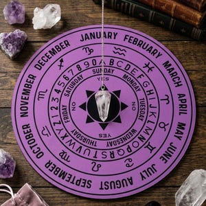 May include: A circular purple dowsing board featuring the months of the year, zodiac symbols, days of the week, numbers zero through nine, and the alphabet. A clear crystal pendulum hangs from a silver chain over the center of the board.