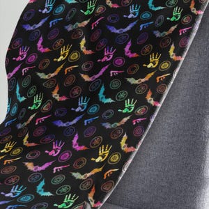 May include: A black blanket with a repeating pattern of colorful handprints, bats, and circular designs. The handprints, bats, and circular designs are in shades of pink, purple, blue, green, yellow, and orange. The blanket is draped over a gray chair.