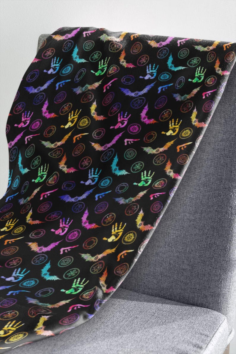 May include: A black blanket with a repeating pattern of colorful handprints, bats, and circular designs. The handprints, bats, and circular designs are in shades of pink, purple, blue, green, yellow, and orange. The blanket is draped over a gray chair.