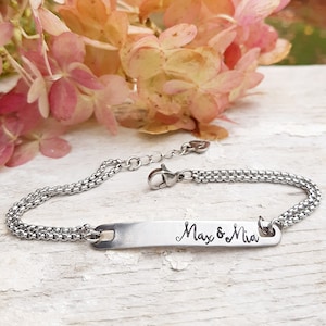 Op de afbeelding: Een zilveren kettingarmband met een gepersonaliseerde bar-bedel gegraveerd met de namen "Max & Mia".